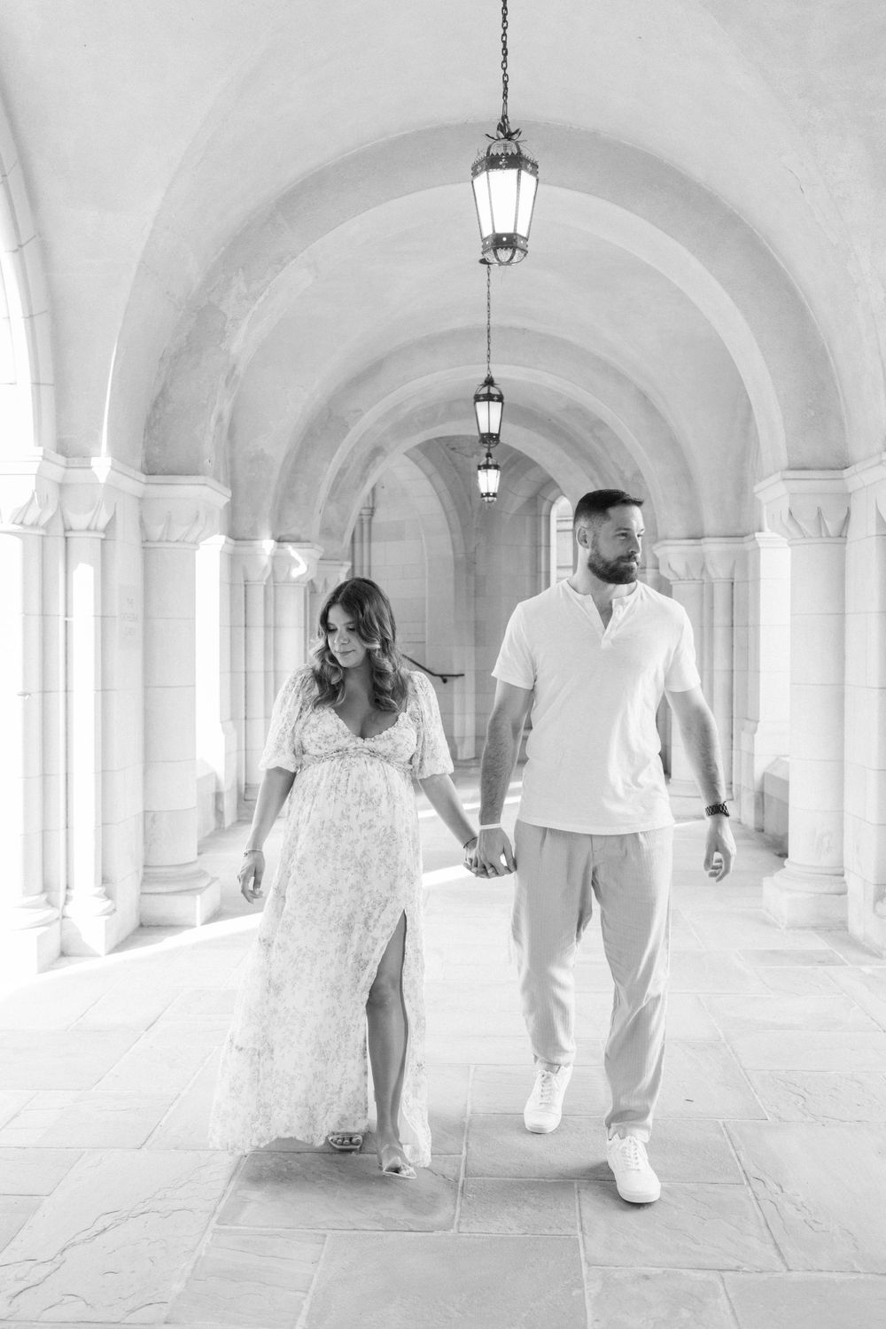 Couple walking hand in hand through elegant arched corridor.