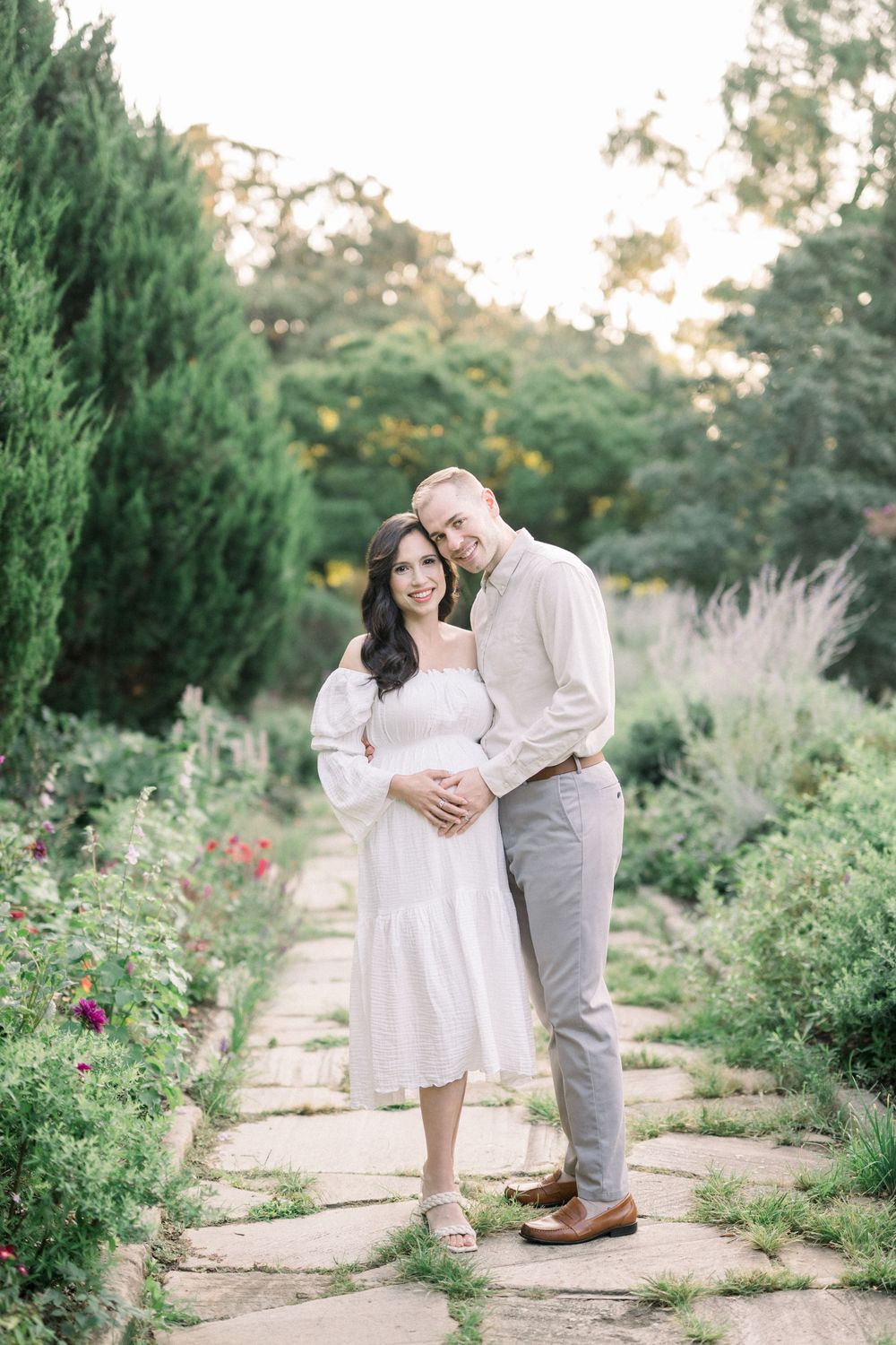 A couple shares tender moments together in a garden pathway surrounded by lush greenery and blooming flowers.