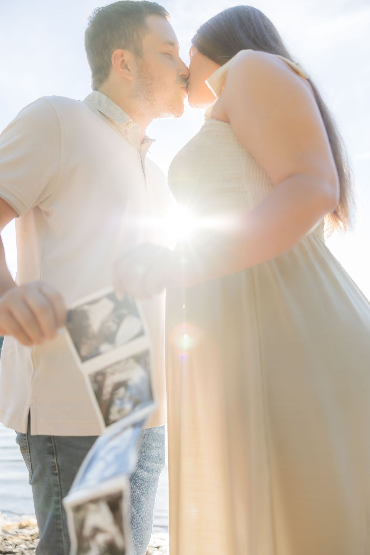 A loving couple embraces and kisses during a romantic sunset photoshoot by the beach.