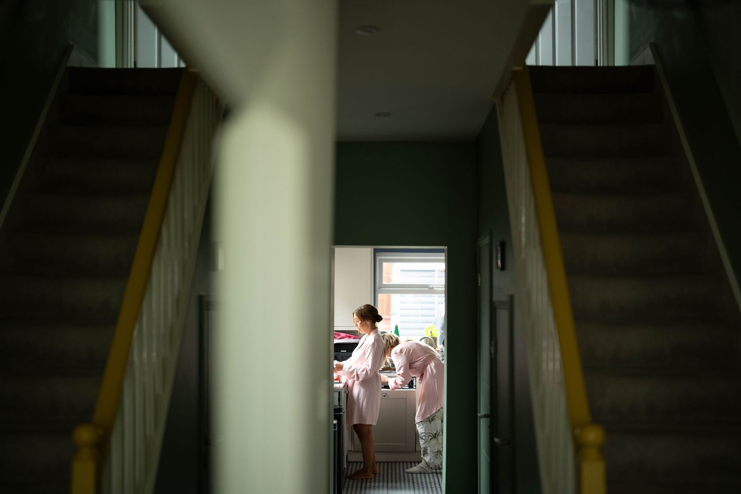 View through a stairwell showing a soft light illuminating a doorway at the end of a hallway.