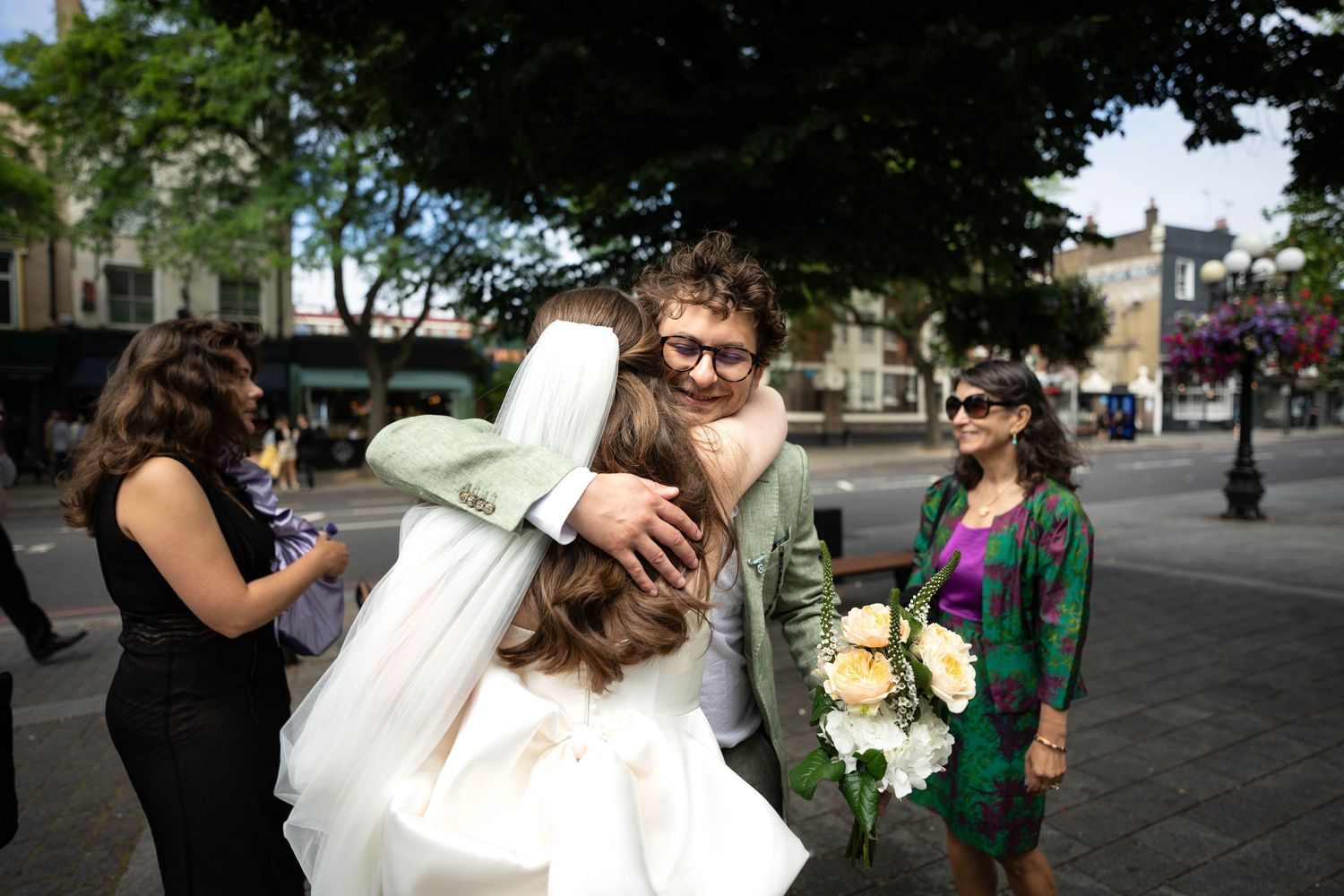 Wedding celebration on a sunny city street with guests gathered around a couple.