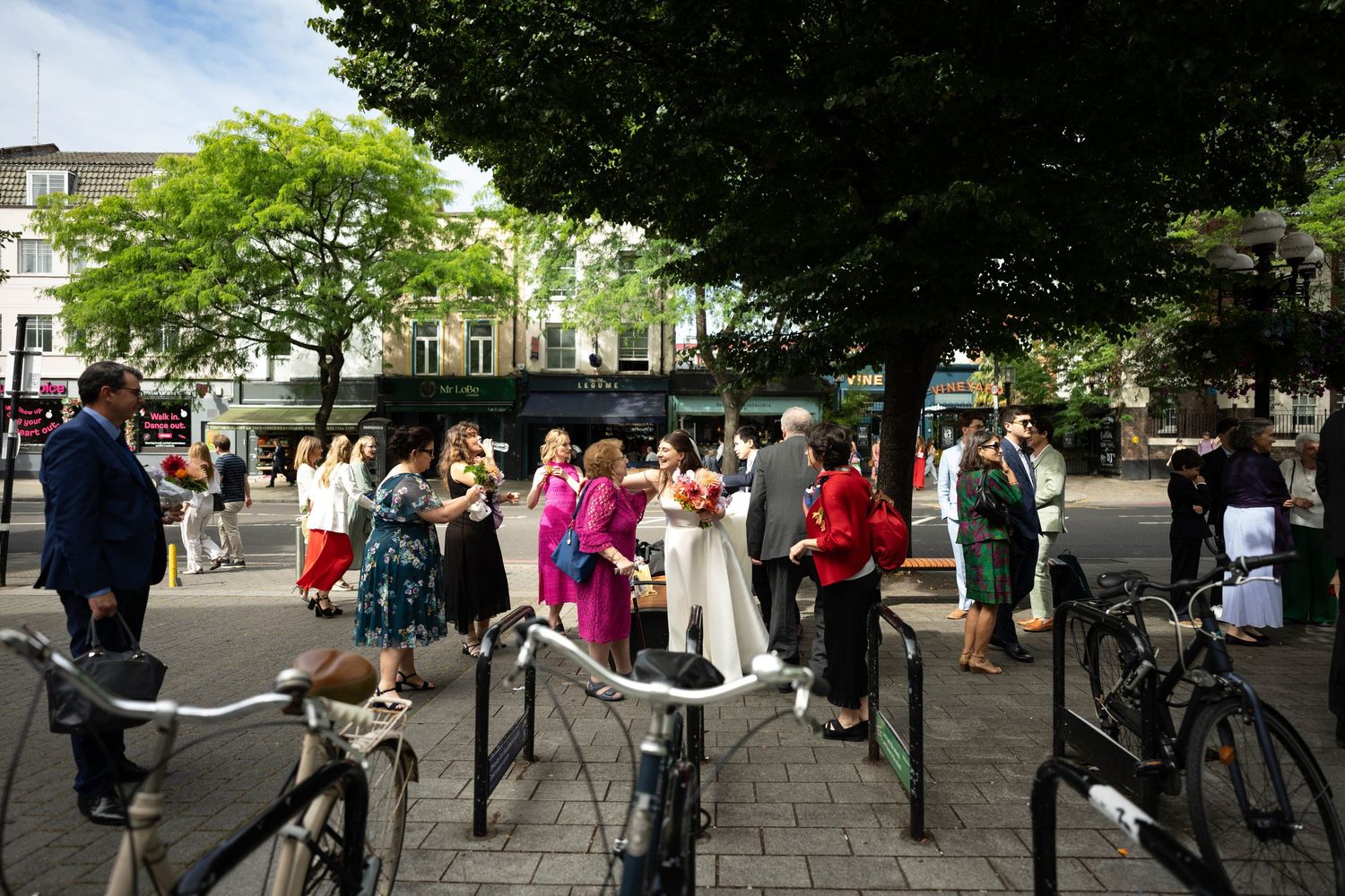 Wedding celebration gathering outdoors with bicycles parked in the foreground on a sunny day.