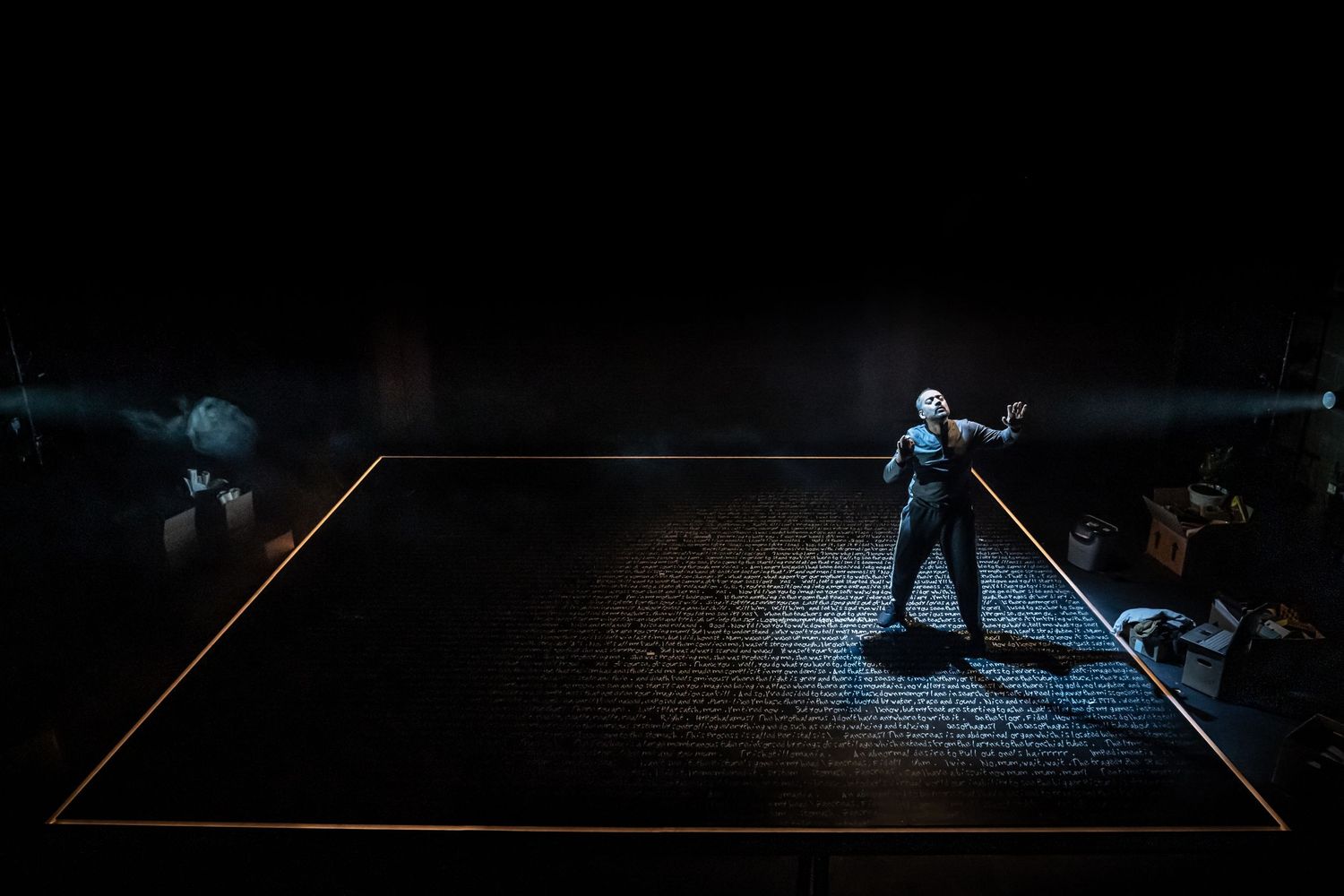 Minimalist stage performance with single spotlight on performer against dark background.