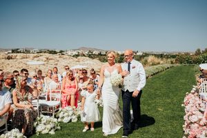 Outdoor wedding ceremony on a hilltop with coral-colored decor and white chairs against a bright blue sky.