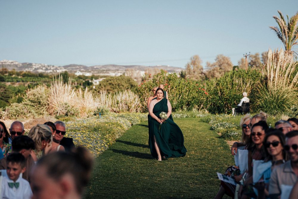 Panoramic view of an outdoor wedding ceremony with guests seated on a grassy hillside overlooking mountains at sunset.