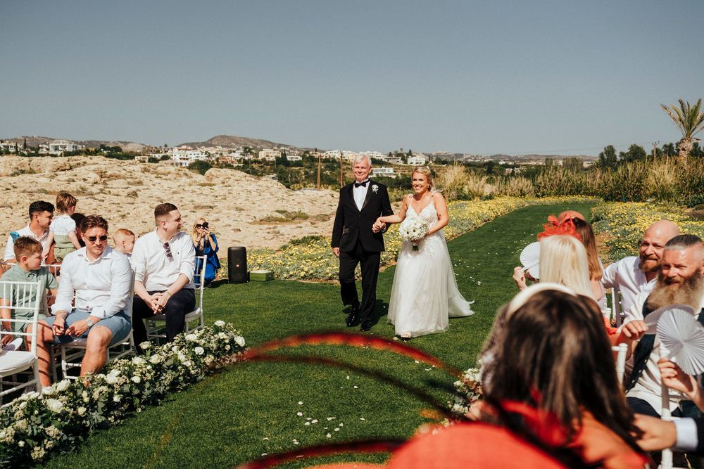 Panoramic view of an outdoor wedding ceremony on a lush green golf course with guests seated in white chairs.