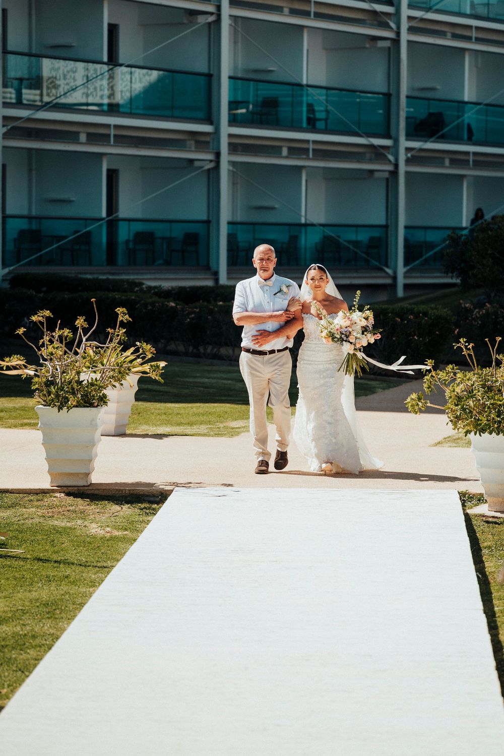 A sequence of wedding photos showing a couple walking behind a white wall with decorative planters in an outdoor setting.