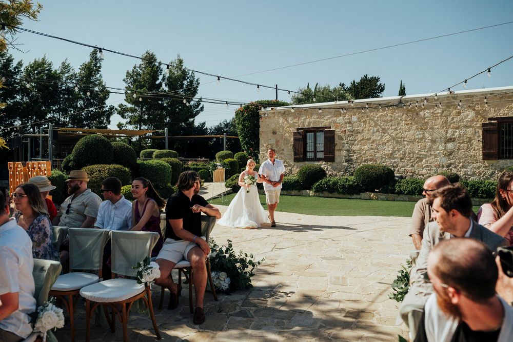 Outdoor wedding reception at rustic stone venue with string lights and guests mingling during sunset.