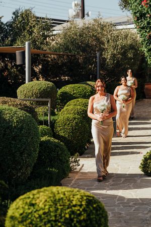A couple walks through a garden pathway with rounded topiary bushes and stone pavers on a sunny afternoon.