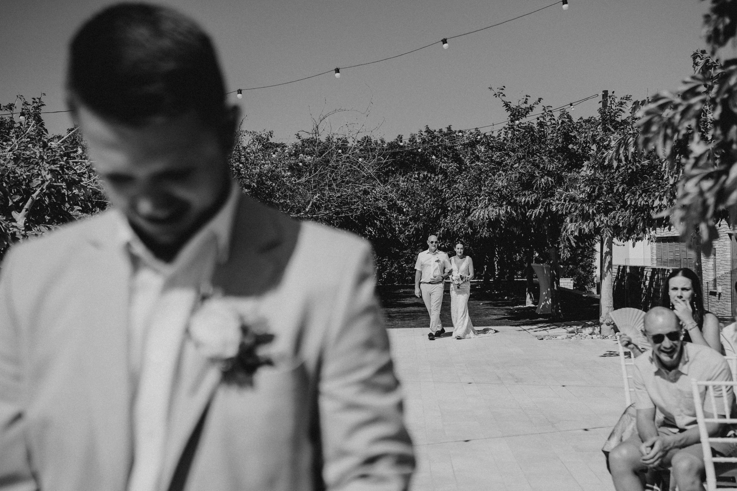 Black and white wedding photo showing outdoor garden ceremony with string lights and guests in the background.