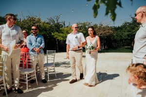 A group of wedding guests dancing in a line on an outdoor terrace during a sunny celebration.