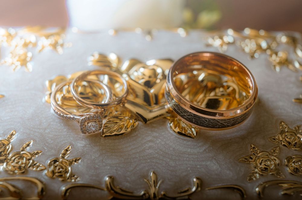 Gold wedding rings and engagement jewelry arranged on a textured gray surface with soft lighting effect.