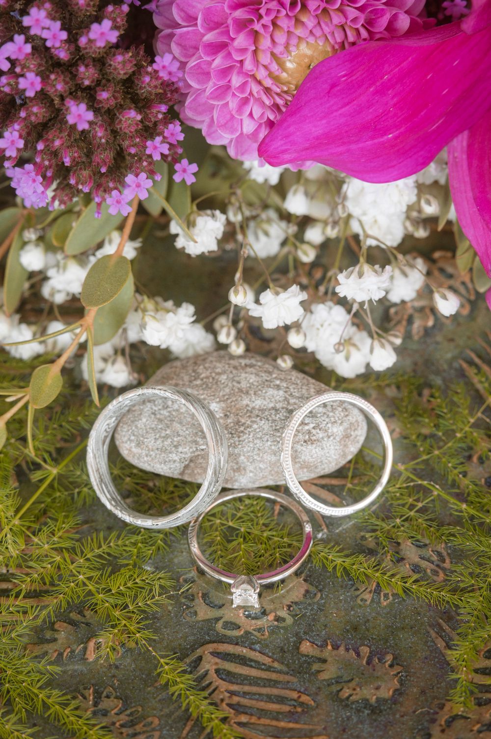 Wedding rings sparkle on green moss surrounded by delicate pink flowers and white baby's breath in a romantic display.