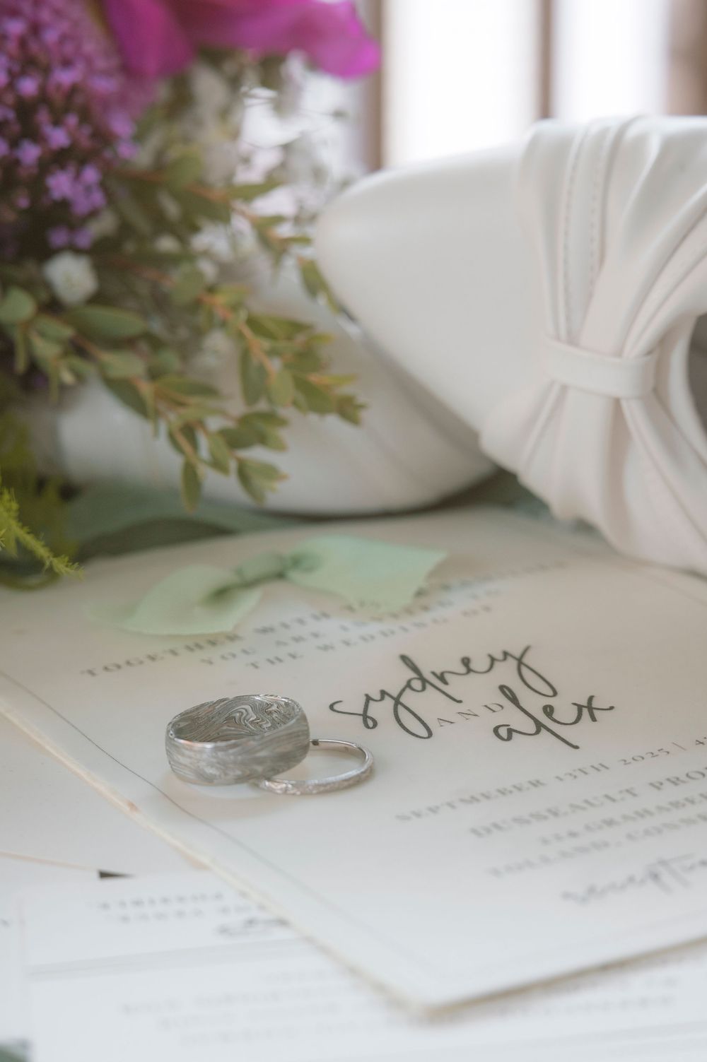 Wedding invitation on white table with delicate purple flowers and handwritten calligraphy details.