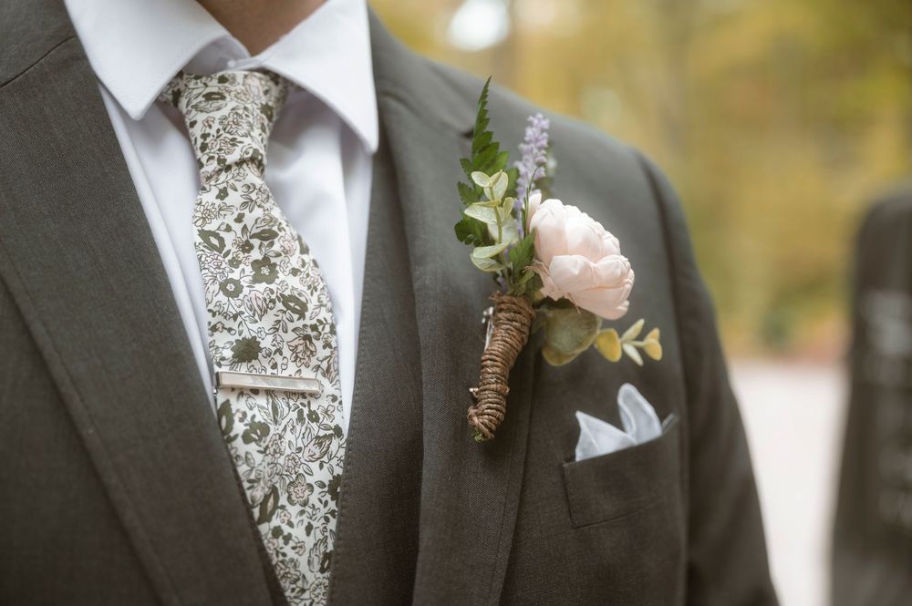 Four elegant gray and white floral patterned neckties with boutonnières adorning formal suits at a special occasion.