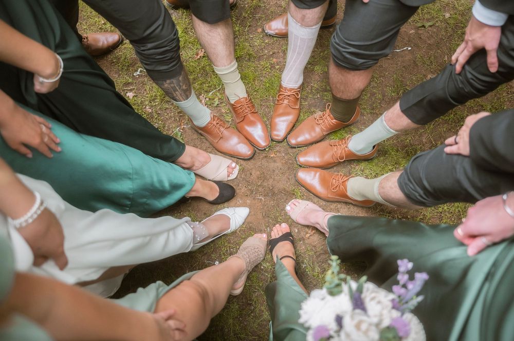 A group of wedding guests stand in a circle showing off their shoes in various styles and colors.