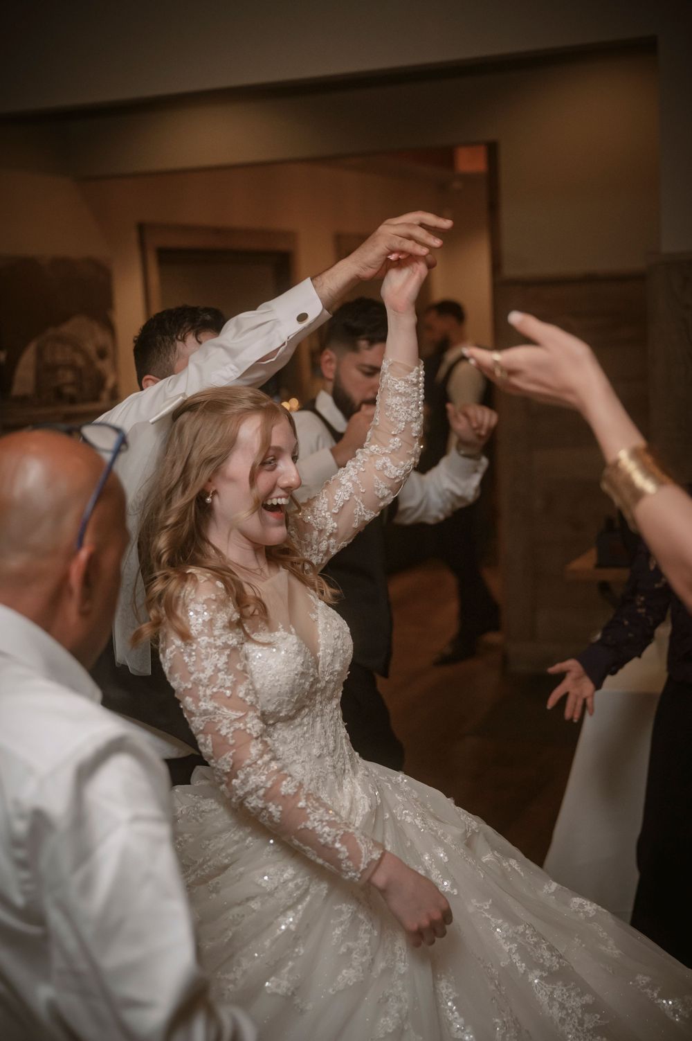 Bride in lace gown laughing and dancing joyfully with guests at wedding reception celebration.
