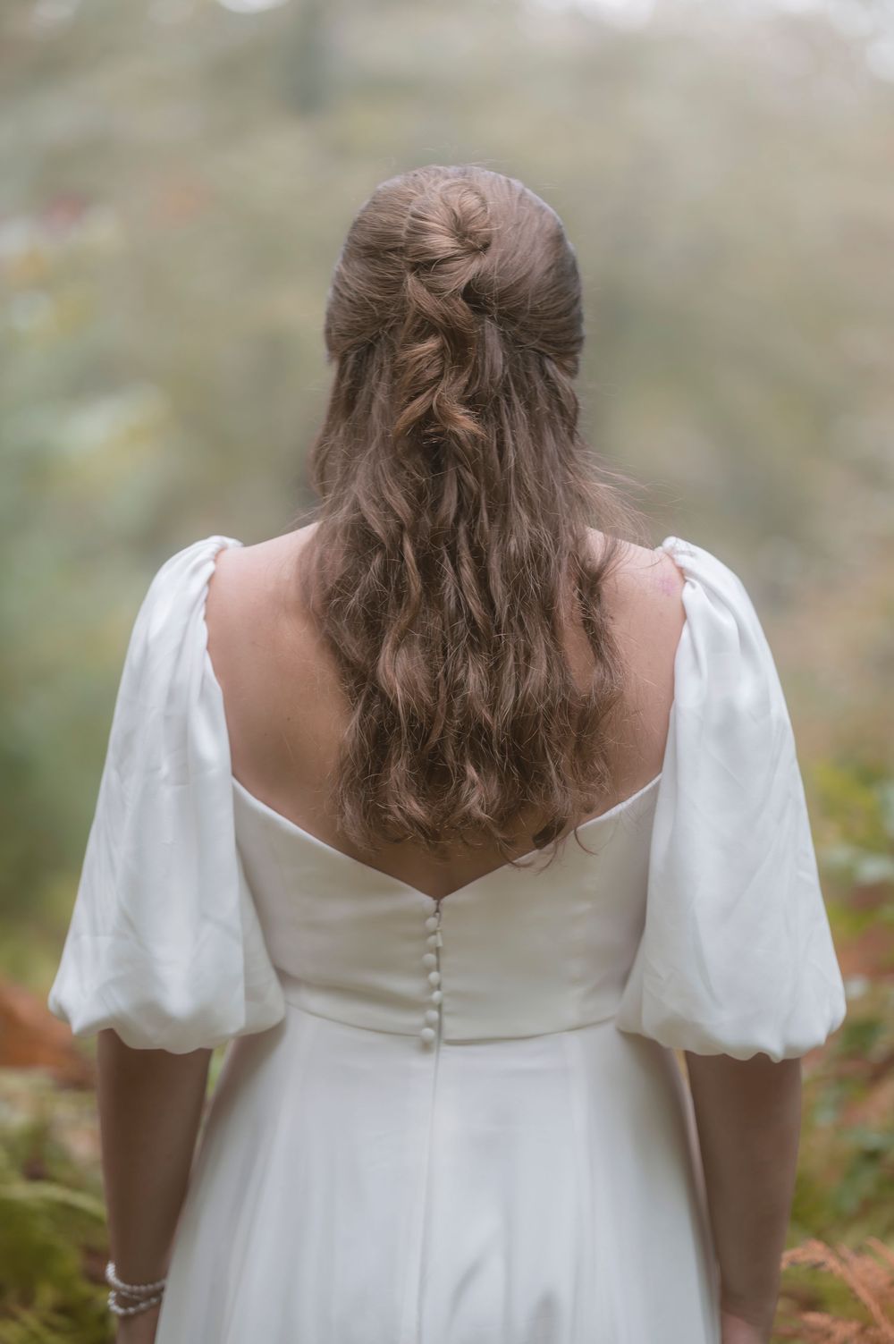Back view of a vintage-style wedding dress with puff sleeves and flowing brown hair styled in romantic waves.