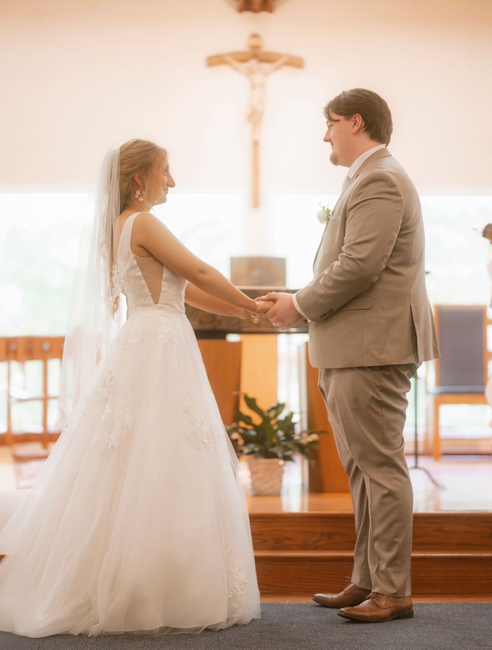A couple exchanges vows during their wedding ceremony in a church with a crucifix and warm lighting.