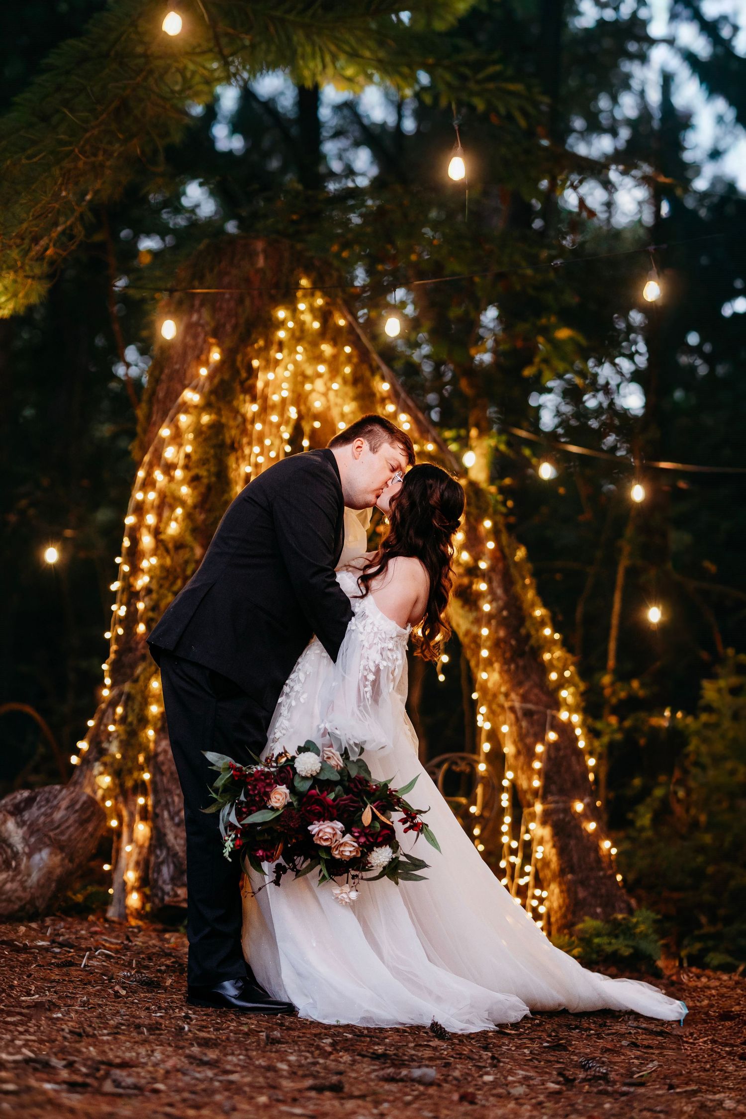 A couple shares a romantic dip kiss beneath a glowing arch of string lights at Wildflower Farm in Greenville, TN.