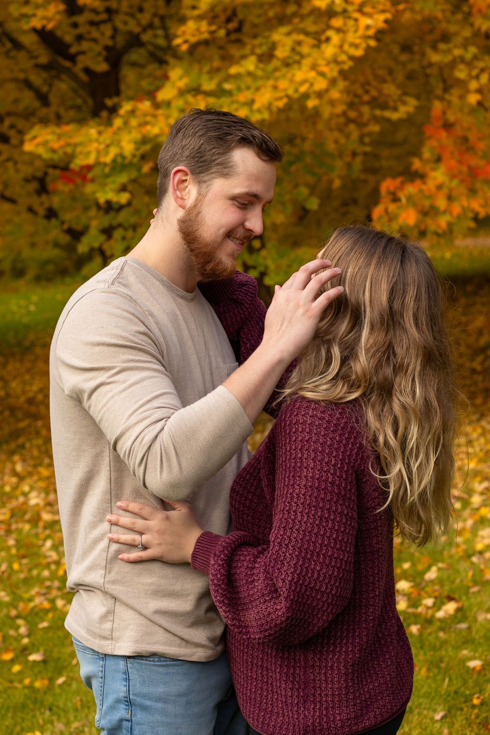 Romantic autumn photo of couple embracing outdoors with golden fall foliage in background.