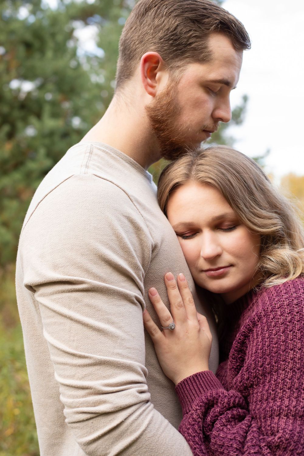 A tender romantic moment between a couple embracing outdoors, with her in a burgundy sweater and him in beige.