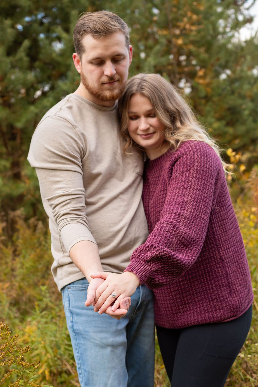 A couple in cozy fall sweaters holding hands and embracing in front of autumn foliage.