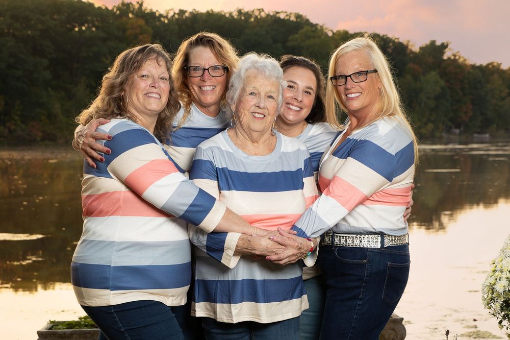 Group wearing coordinated navy and coral striped outfits poses for sunset family photos by a serene lake.