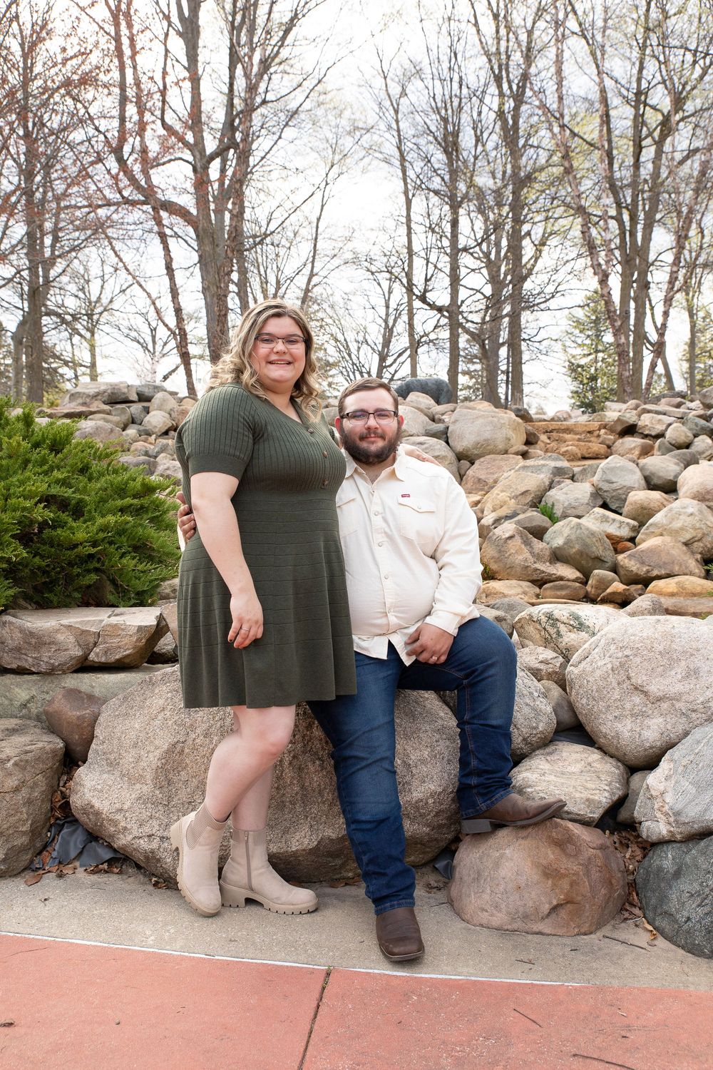 A couple sits together on large decorative boulders along a landscaped pathway on a cloudy day.