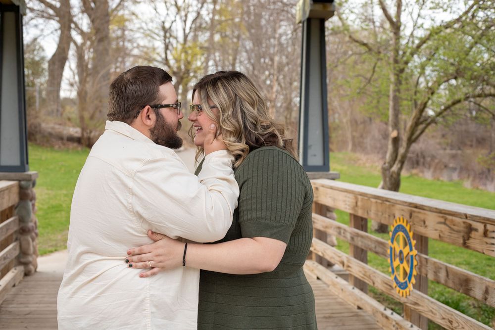 A couple shares a romantic moment along a wooden bridge surrounded by autumn trees during their engagement photo session.
