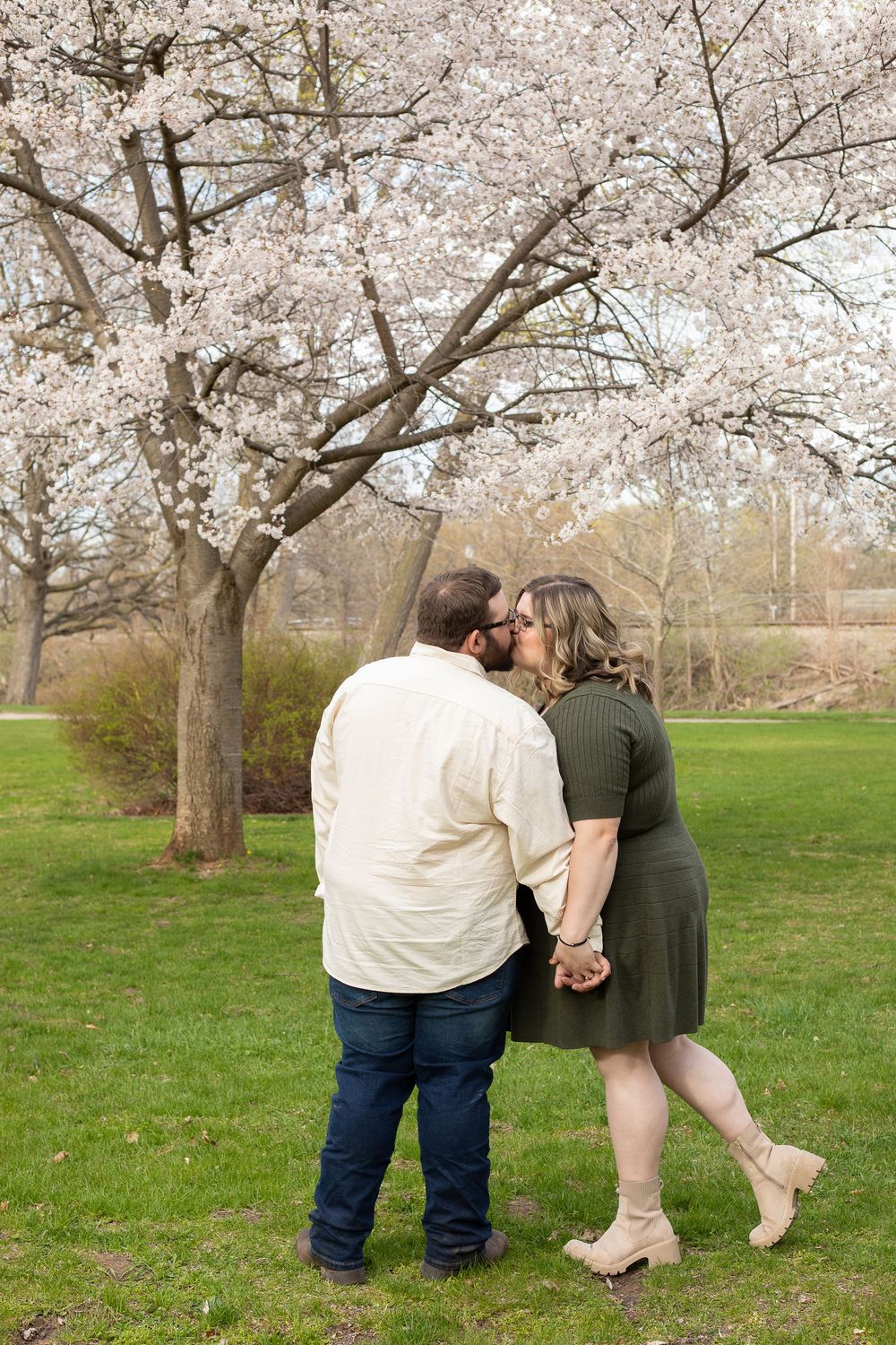 A couple shares a romantic moment under blooming cherry blossom trees in a spring park setting.
