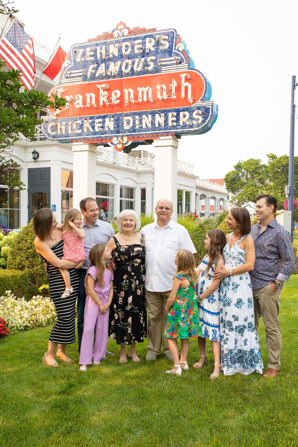 Vintage Zehnder's Famous Frankenmuth Chicken Dinners neon sign stands above a group gathered on manicured lawn.
