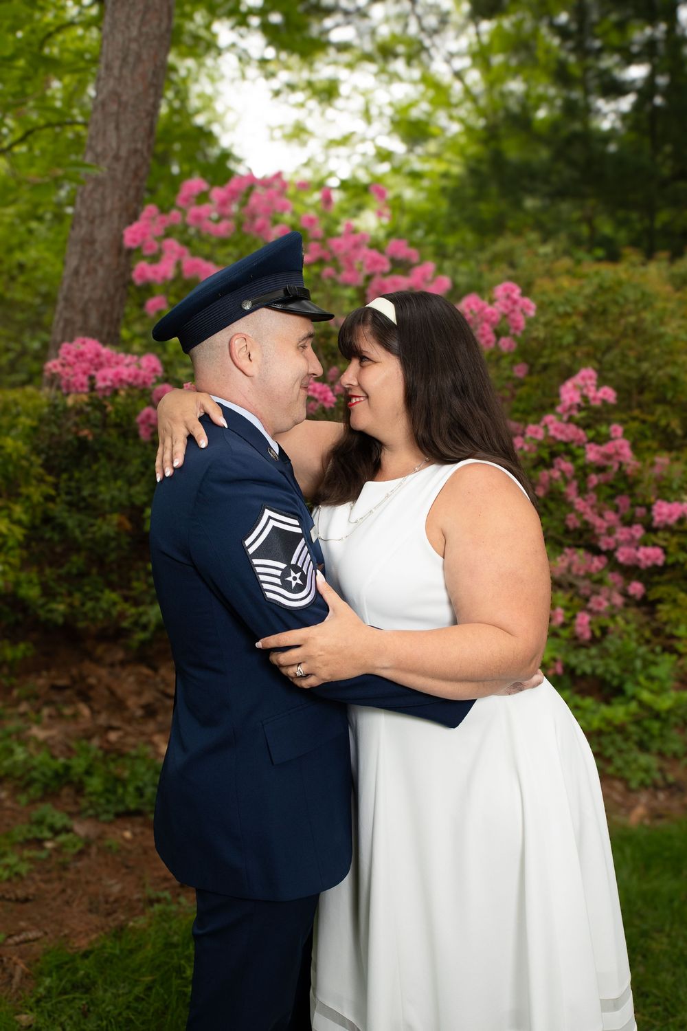 A romantic couple embraces outdoors with blooming pink azaleas in the background during a wedding photo session.