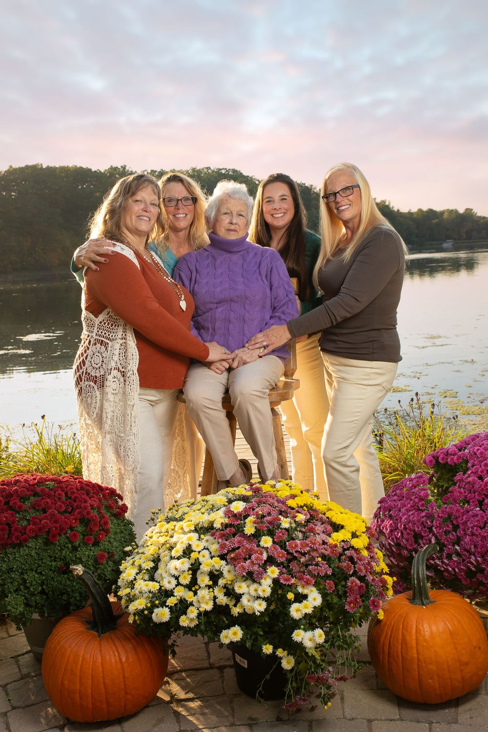 A group photo by a lake with colorful mums and pumpkins decorating the foreground at sunset.