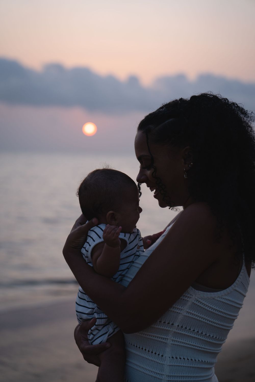 Maman portant son enfant sur la plage au coucher du soleil en Guyane
