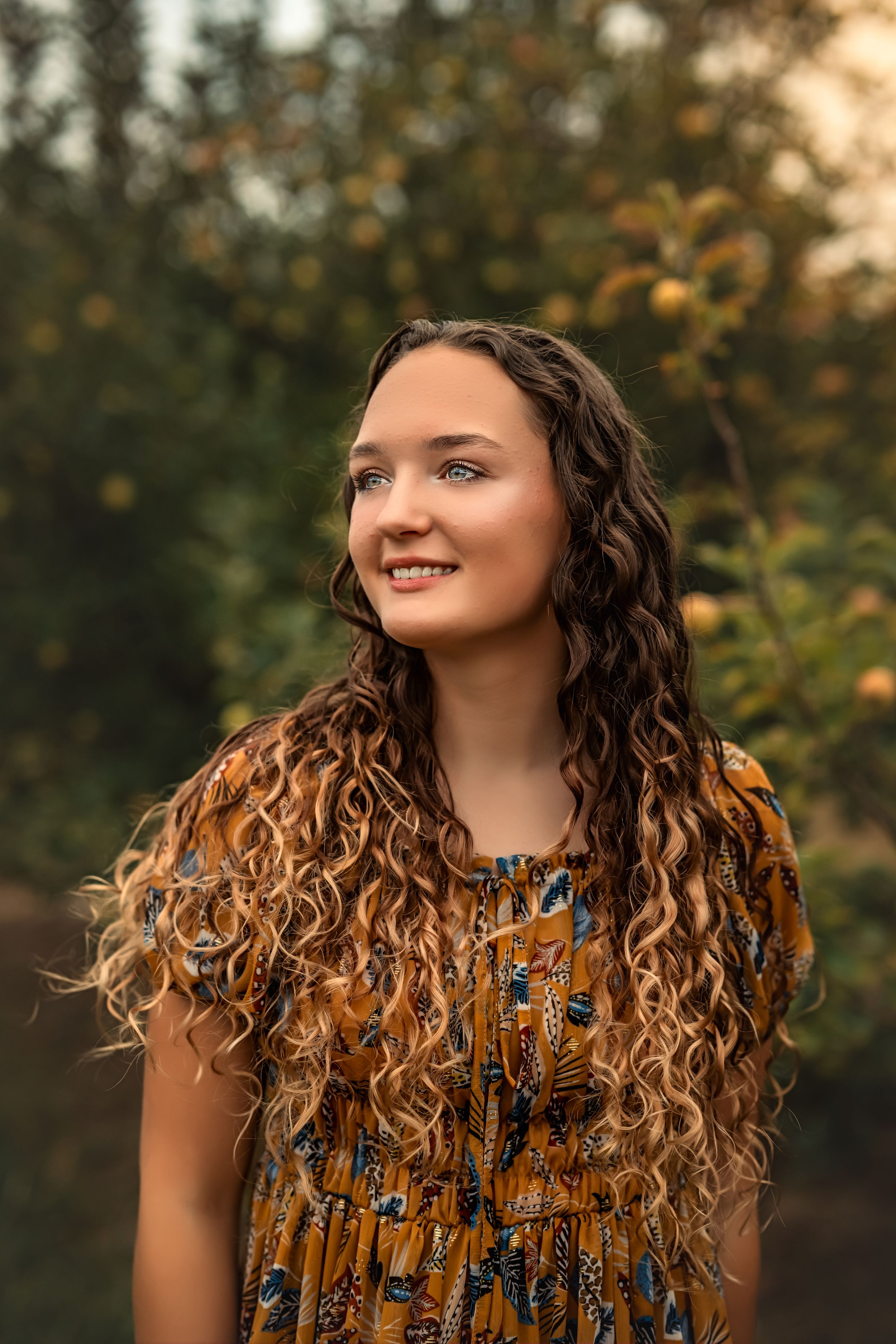 A senior girl with long curly blonde hair poses outdoors during golden hour for senior photos.