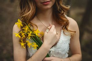 Senior girl holds a bouquet of bright yellow daffodils against a white lace dress in a romantic outdoor setting.
