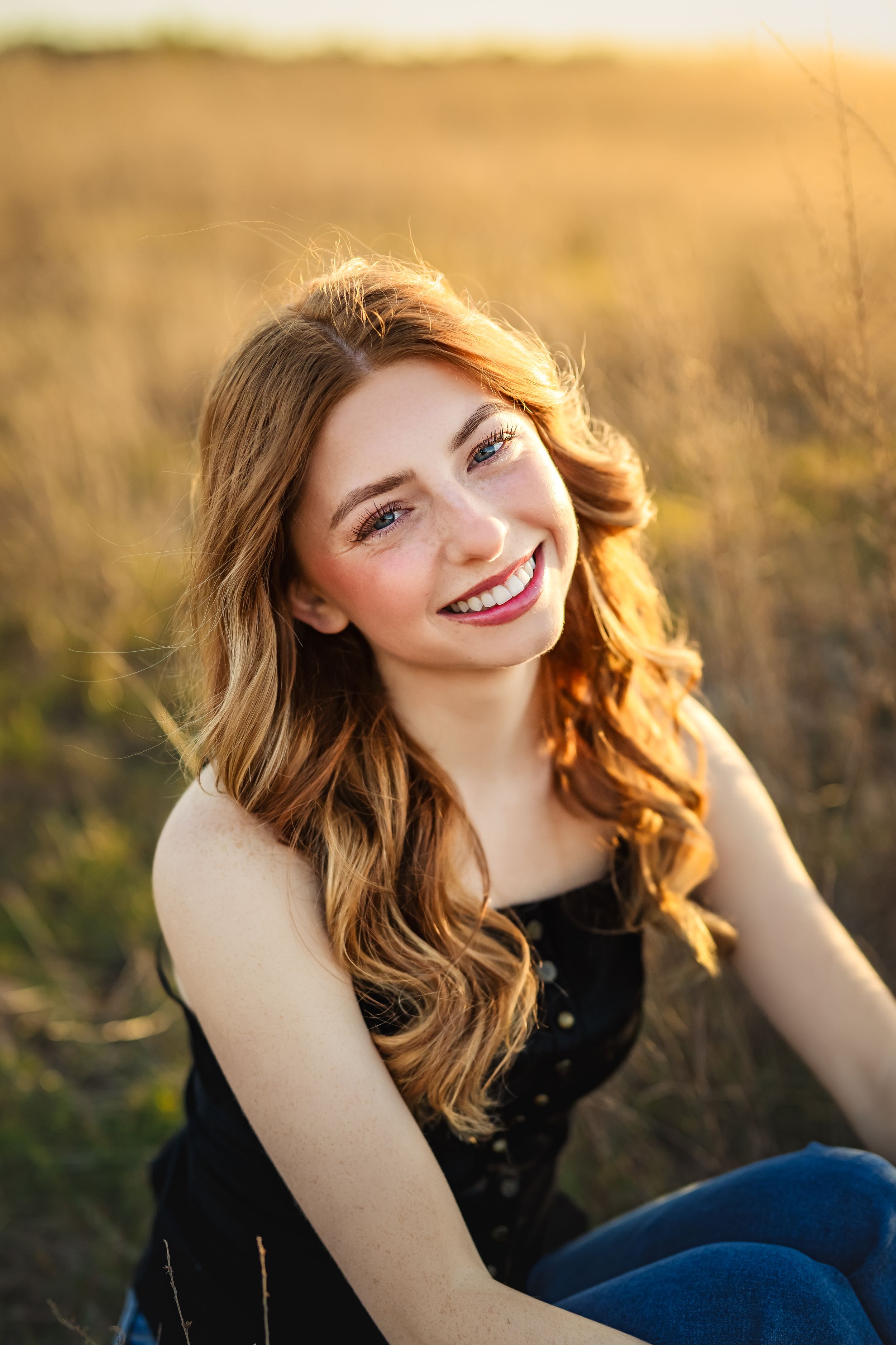 A portrait of a smiling senior girl with red curly hair and freckles in golden sunlight during an outdoor Chattanooga senior photo session.