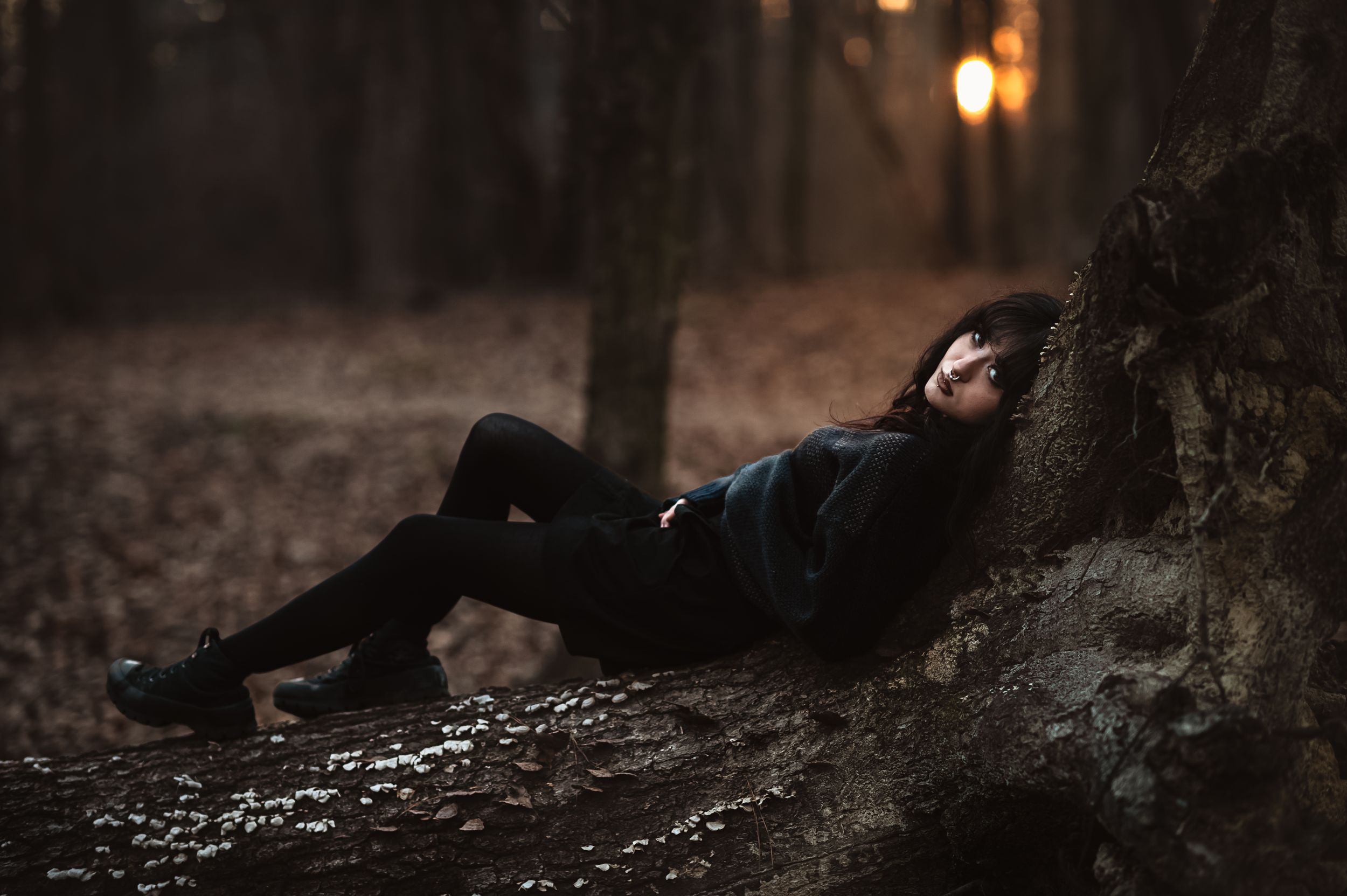 goth teenage girl lies on fallen tree in a dark winter forest for senior photos