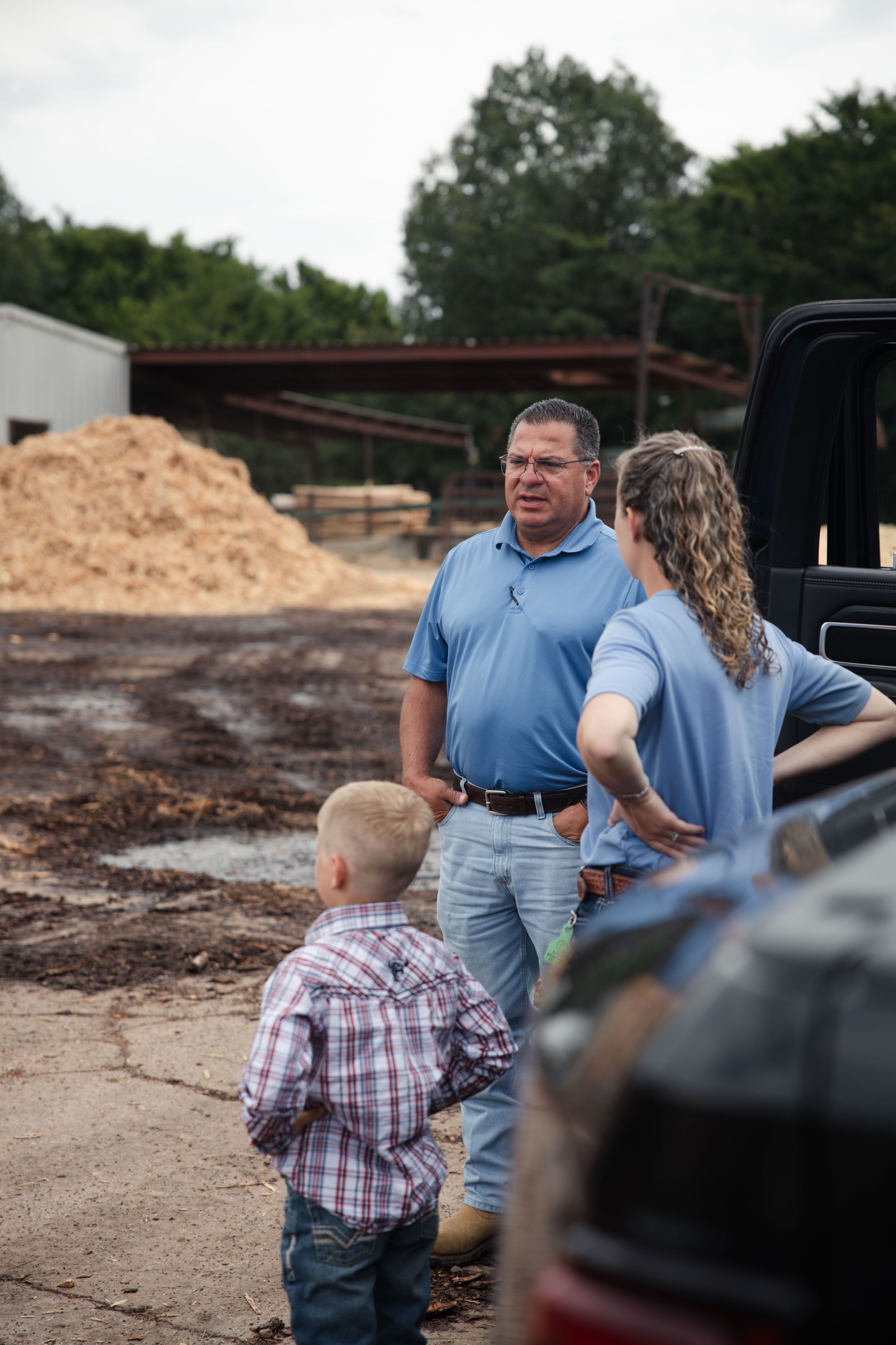 People standing near a pickup truck at a construction site with a pile of sawdust in the background.