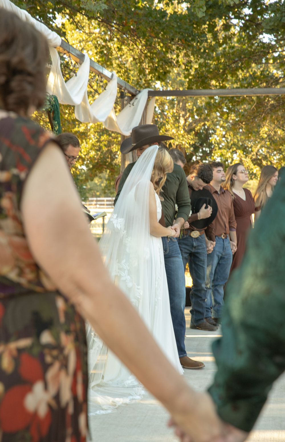 Bride in white dress and cowboy hat with wedding veil at outdoor rustic country wedding ceremony.