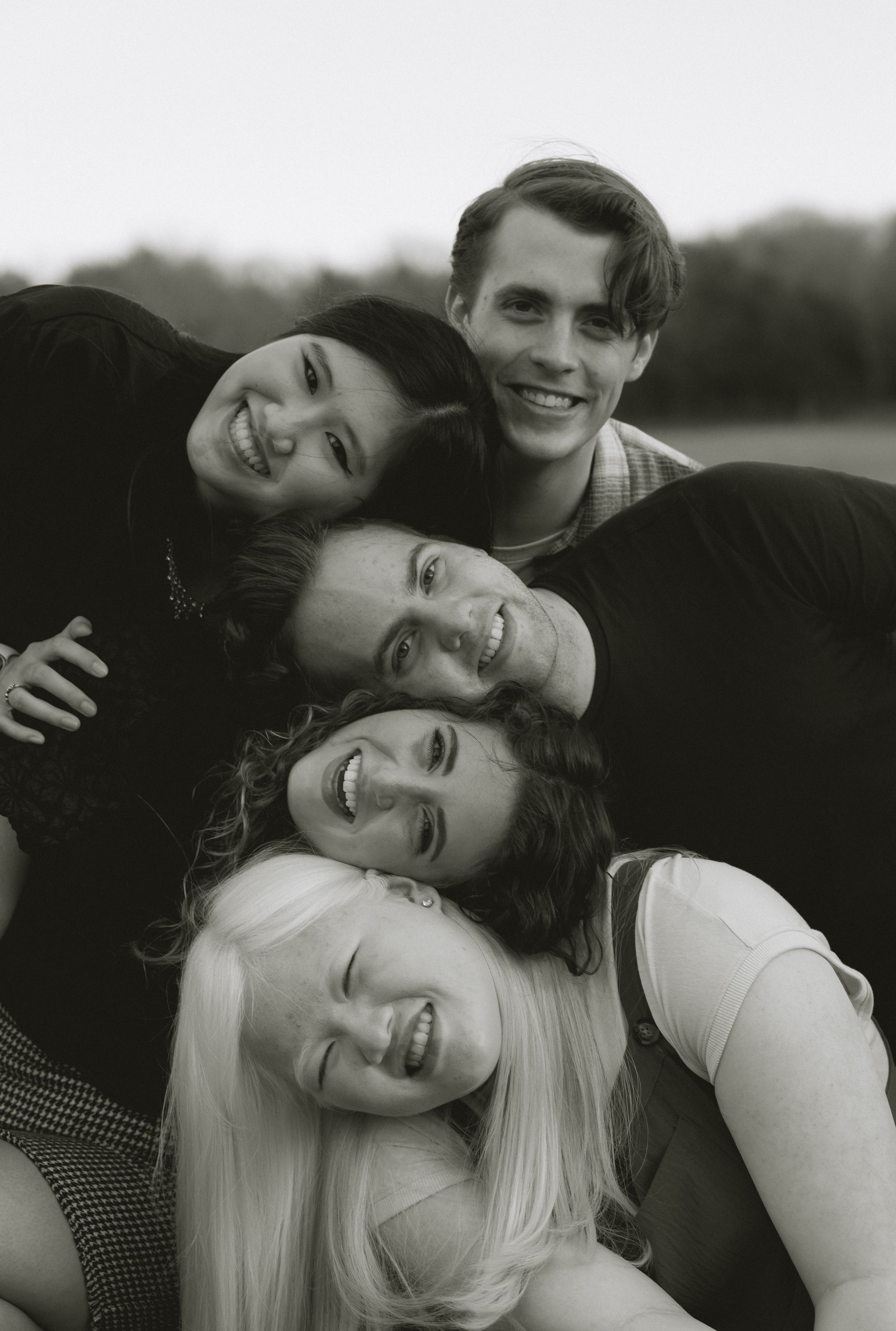 Black and white portrait of four smiling young friends stacked together in a playful outdoor group photo.