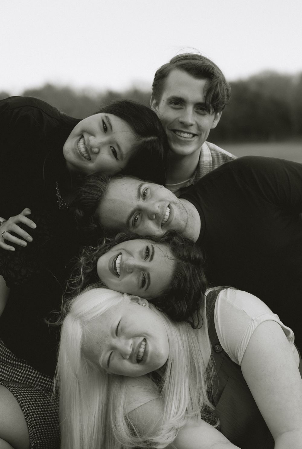 Black and white portrait of four smiling young friends stacked together in a playful outdoor group photo.