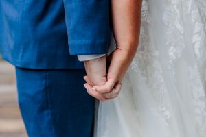 Close-up of couple holding hands showing wedding dress and blue suit details.