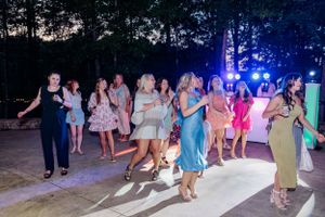 Wedding guests dancing together on an illuminated outdoor dance floor at night with blue lighting.