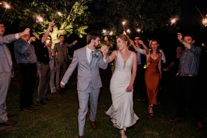 Newlyweds exit reception under sparkler send-off at night.
