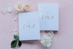 Elegant wedding vow books with calligraphy on pink background with rose petals.