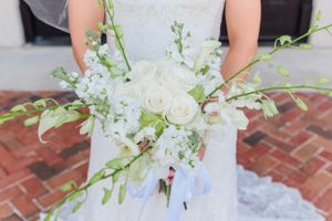 White wedding bouquet with roses and delicate greenery held against brick background.
