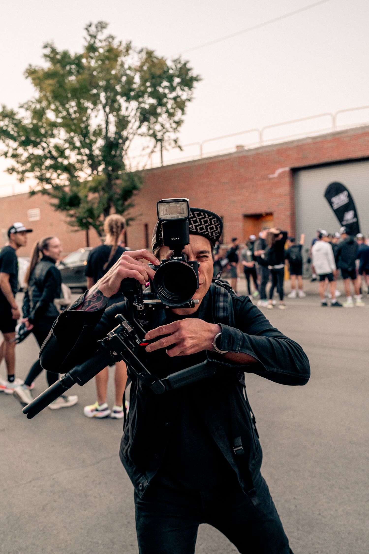 Professional photographer wearing black gear captures photos on a DSLR camera in an urban outdoor setting.