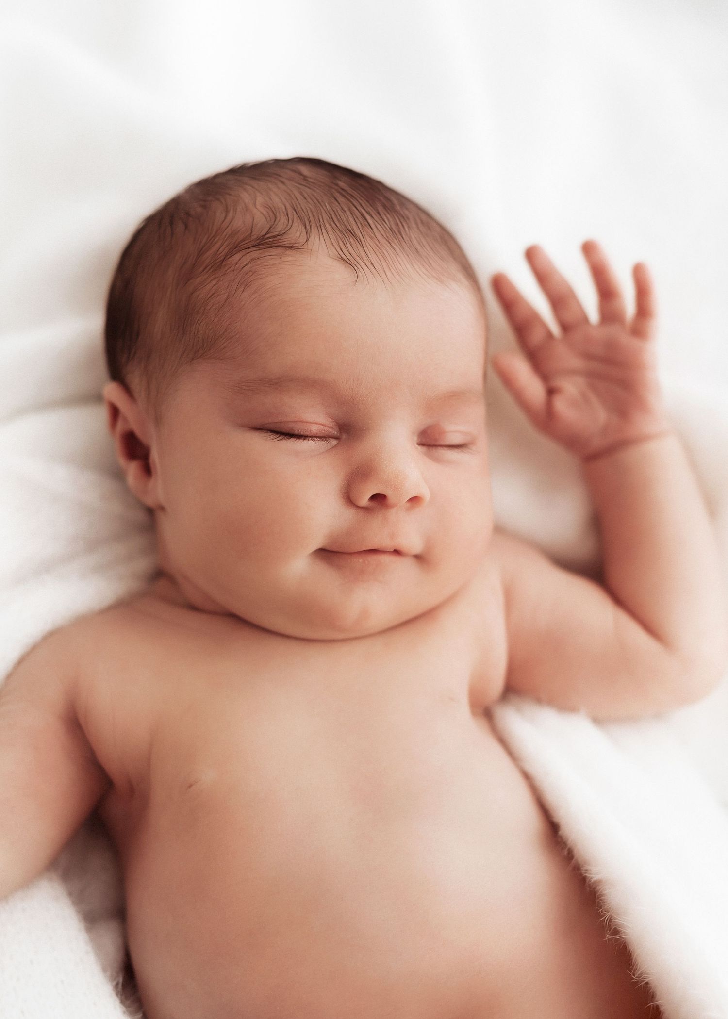Happy baby in peach romper sitting and laughing against white backdrop.